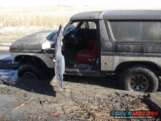 1985 Ford Bronco stuck in mud, driver's door open, red interior visible