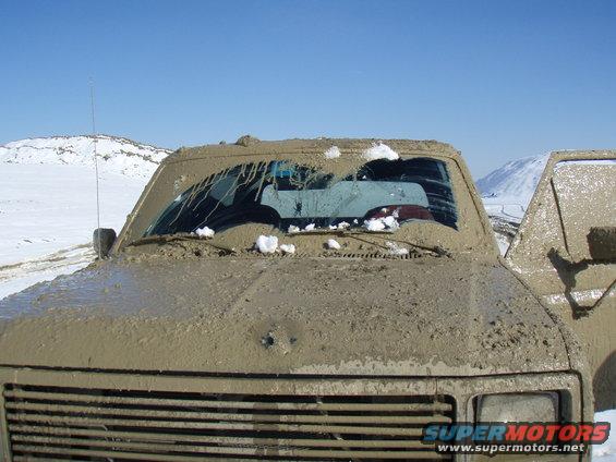 Mud-covered 1985 Ford Bronco front end with snow on windshield. Another vehicle is visible to the right