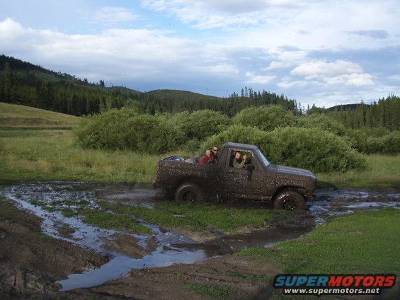 Mud-covered SUV driving through a muddy field with people inside
