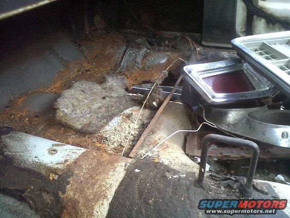Rusted interior floor pan with exposed insulation and a red taillight assembly in a vehicle