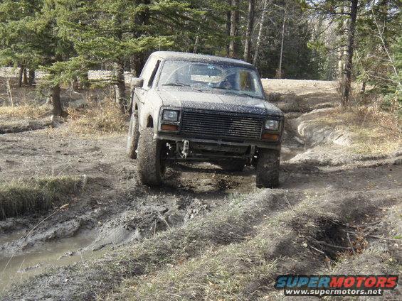 Muddy 1980s 4x4 truck navigating a dirt track with trees in background