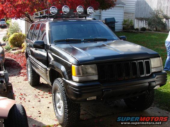 Black Jeep Grand Cherokee with roof lights and off-road tires parked outside