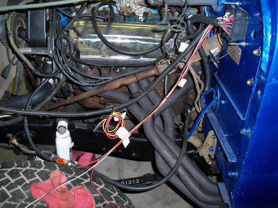 Engine bay with chrome valve covers, black exhaust manifolds, and blue fender. Wires and hoses are visible