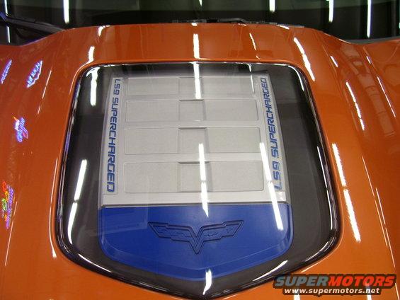 Orange car hood with a clear panel showing an engine cover with LS9 SUPERCHARGED text and a Corvette emblem