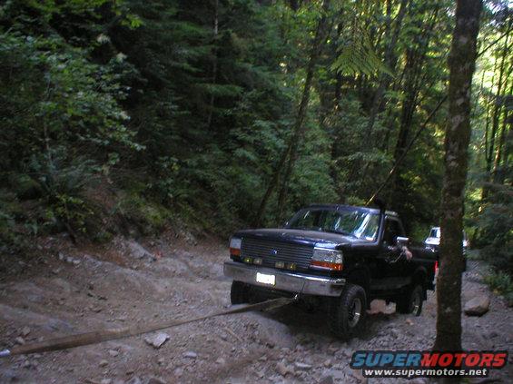 Black pickup truck being towed on a dirt road in a forest