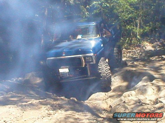 Blue SUV with large tires going over rocks, smoke coming from behind it