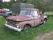 1966 Ford F-250 - A weathered Ford F-series truck sits in overgrown grass next to other vehicles and a large tarp-covered structure.