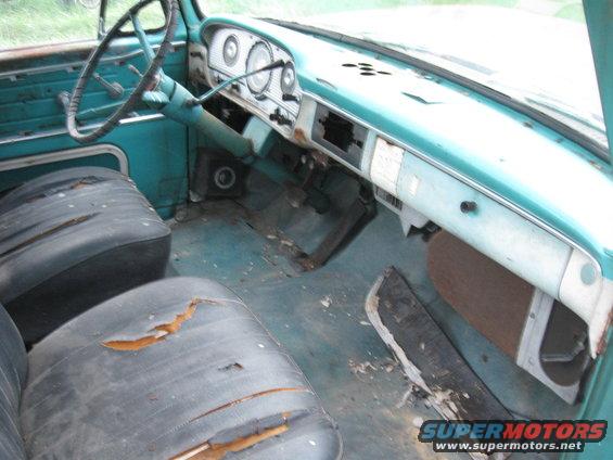 Turquoise truck interior with torn black vinyl seats, cracked dashboard, and visible floor debris