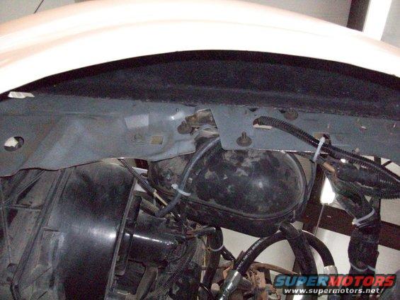 Close-up of vehicle engine bay showing brake booster and various hoses and wiring