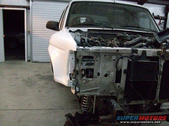 White truck front end disassembled, showing engine bay and chassis components