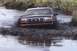 1993 Ford Bronco - A Ford truck navigates a muddy trail, kicking up water and mud.