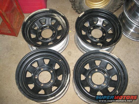 Four black steel wheels with eight lug holes, stacked in pairs