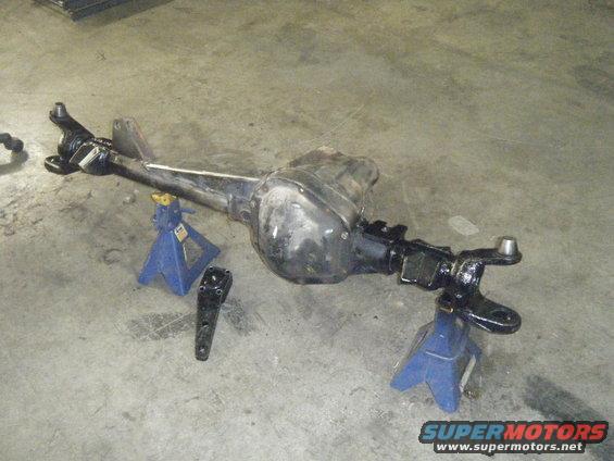 Rear axle assembly resting on two blue jack stands with a separate bracket on the floor