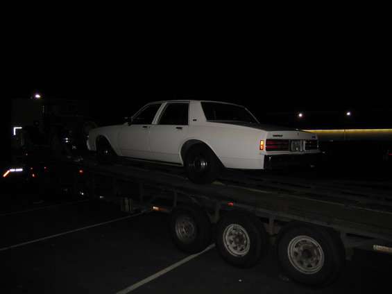 White sedan on car carrier, rear view. Appears to be 1980s model