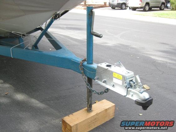 Boat trailer tongue with blue frame, silver coupler, jack, and safety chains on a wooden block