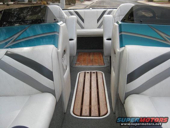 Interior of a boat with white seats and teal accents. Wooden floor panels are visible
