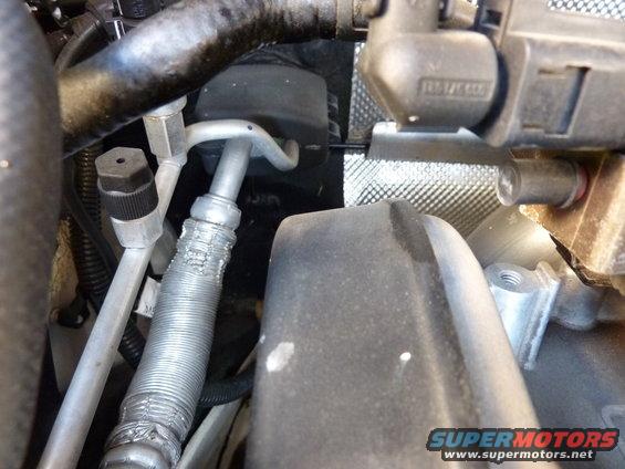 Close-up of engine bay hoses and electrical connectors. Some text is visible on a black component