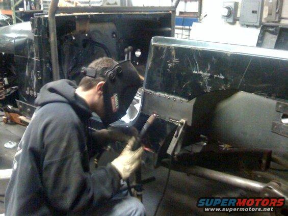 Man in welding mask working on a black Jeep YJ body panel. The panel has been riveted