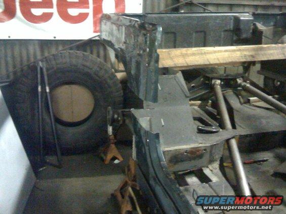 Jeep YJ frame being worked on, spare tire visible. Supermotors.net logo at bottom right