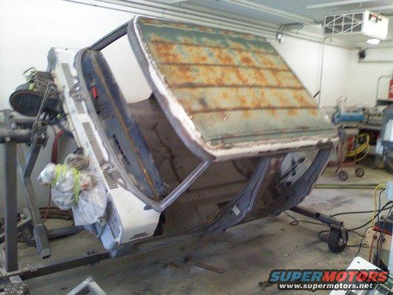 Car body upside down on a rotisserie in a workshop. The roof is rusty