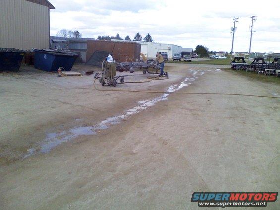 Vehicle frame on a stand with a sandblaster hose and operator nearby