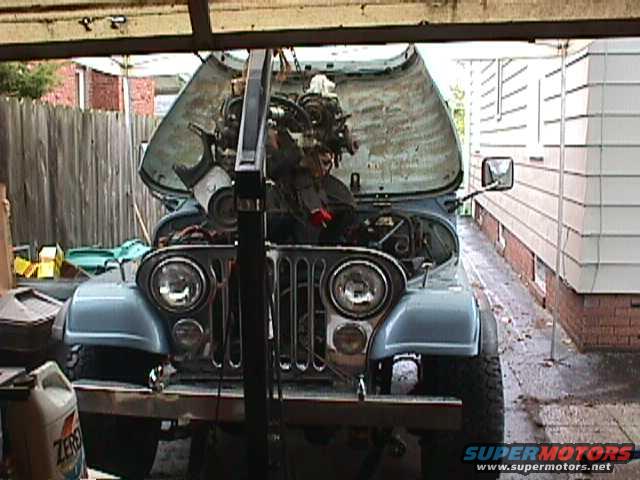 Jeep CJ-7 with hood open, engine being worked on, parked in a driveway