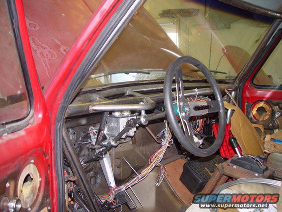 Interior view of a red vehicle with a roll cage, exposed wiring, and aftermarket steering wheel