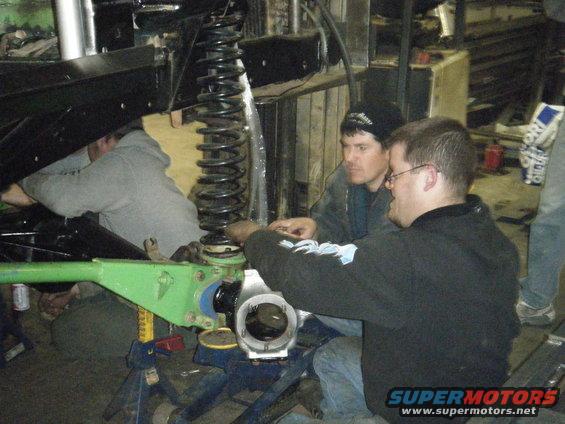 Green suspension component on vehicle under repair, with three men working