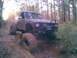 1984 Ford Bronco II - This heavily modified pickup truck is navigating a challenging muddy path through a dense forest.