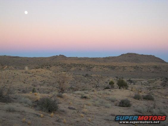 Desert hills under a pink and blue sky with the moon visible
