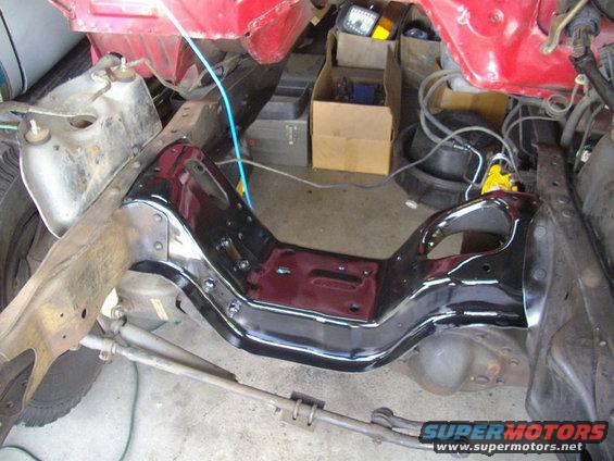 Close-up of a vehicle's frame and suspension components, with some red body panels visible above