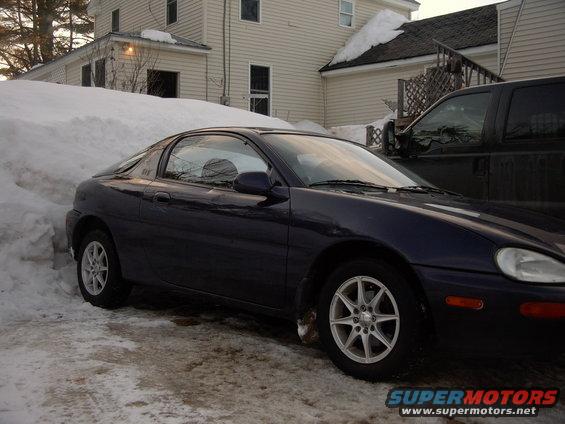 Dark blue 1993 Mazda MX-3 coupe parked in snow next to a black pickup truck