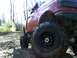 1994 Ford F-250 - This red pickup truck is equipped with large off-road tires and is driving on a muddy trail.
