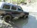 1994 Ford F-250 - A Jeep Cherokee XJ navigates a muddy trail, with another vehicle visible further up the incline.
