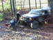 1994 Ford F-250 - A Jeep Cherokee XJ is winched by two people in a wooded area with fallen leaves.