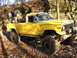 1994 Ford F-250 - A yellow Jeep J-10 pickup truck modified for off-roading navigates a wooded trail.