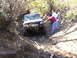 1994 Ford F-250 - A white Jeep Cherokee navigates a muddy, wooded trail with assistance from onlookers.