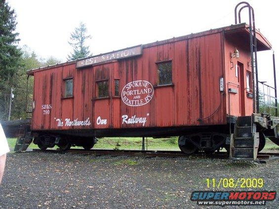 Red caboose with 'BEST STATION' and 'The Northwest's Own Railway' text, on train tracks