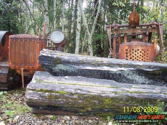 Rusty tractor with large grille and a piece of logging equipment in a wooded area