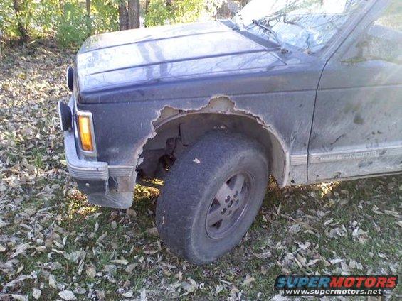 Front fender of a dark blue truck showing significant rust damage. The wheel is visible