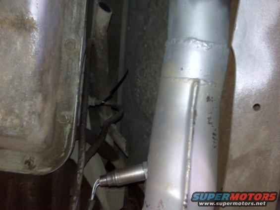 Close-up of an exhaust pipe with an oxygen sensor attached, showing metal components and wiring