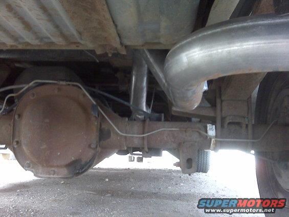 Underside of a truck showing a rusty rear axle, exhaust pipe, and leaf springs