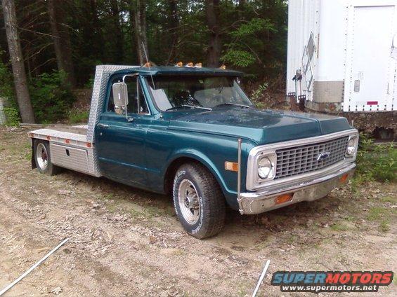 Teal flatbed truck with a chrome grille and diamond plate bed, parked on a dirt lot