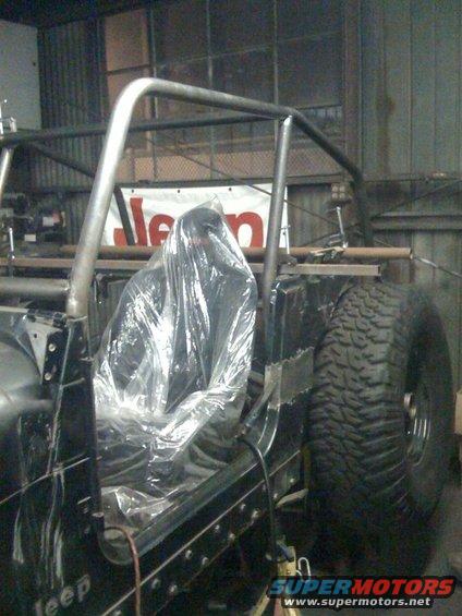 Jeep interior with roll cage and seat covered in plastic. Jeep logo visible on banner in background
