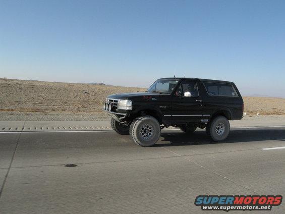 Black Ford Bronco driving on a highway with desert landscape in background