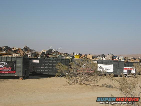 Dumpsters overflowing with debris in a desert landscape under a clear blue sky