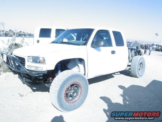 White off-road pickup truck with custom bumper and large tires, another white vehicle behind it
