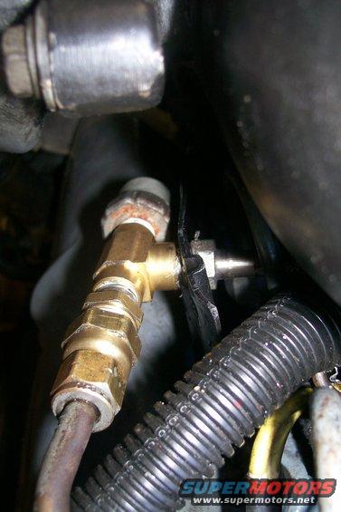 Close-up of a brass fitting connected to engine components and hoses