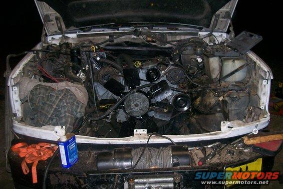 Truck engine bay with engine components visible, tools and a bottle of cleaner on the bumper