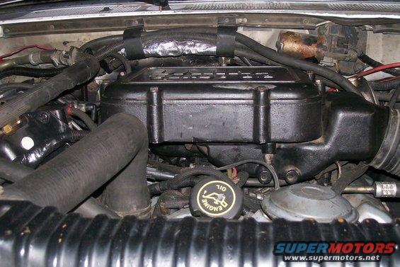 Engine bay with hoses and black engine cover. Oil cap says 'ENGINE OIL'